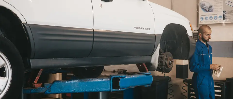 A technician in blue coveralls at a raised white SUV in a shop