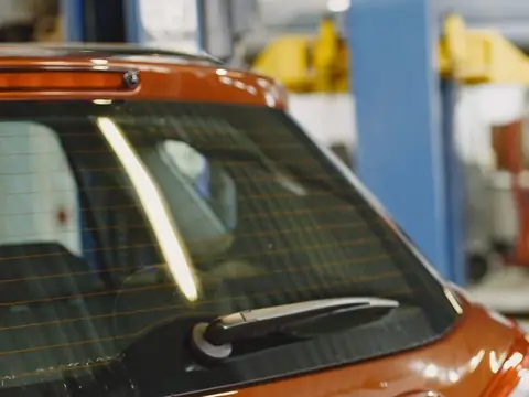 The rear window of an orange hatchback, the defroster lines across the glass