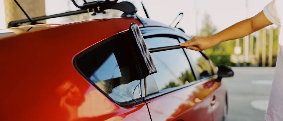 A squeegee drawn down the side window of a red hatchback