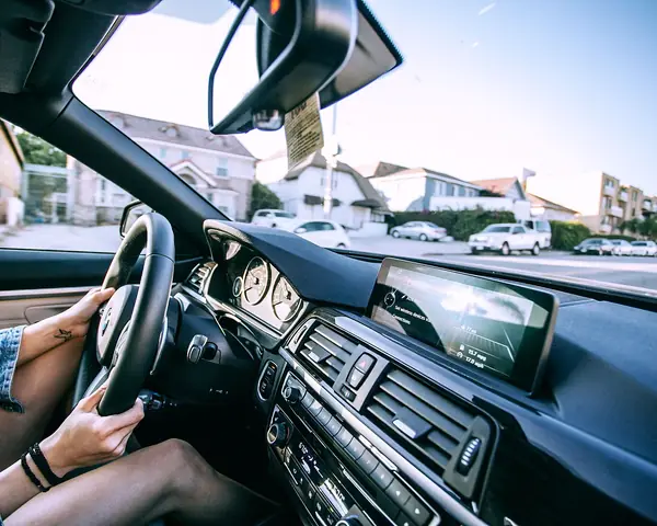 A driver at the wheel on a sunny street, the windshield and mirror ahead