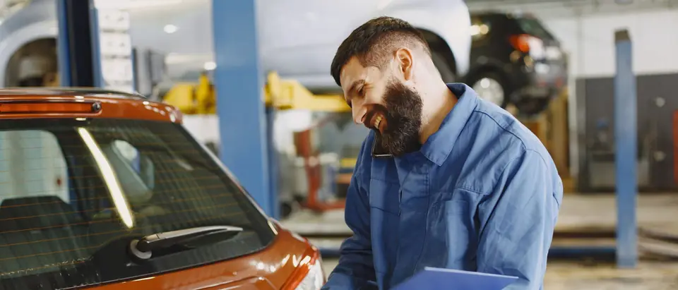 A technician on the phone going through paperwork beside an orange car