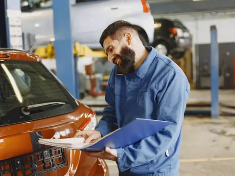 A technician on the phone going through paperwork beside an orange car